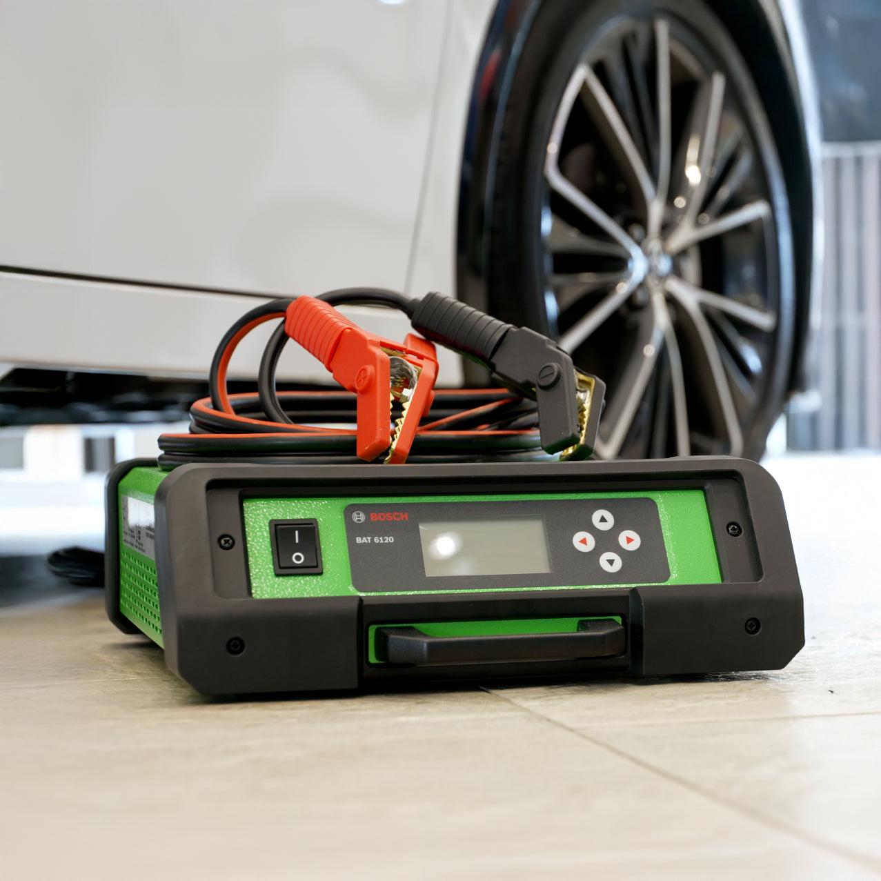 Bosch BAT 6120 sitting on the floor next to a vehicle with the power cables on top of the device.